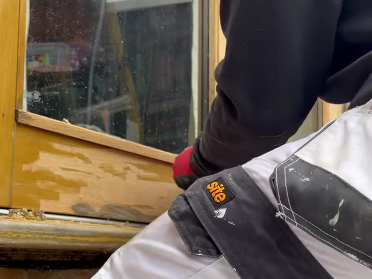 Decorator in white overalls preparing and sanding a timber window frame