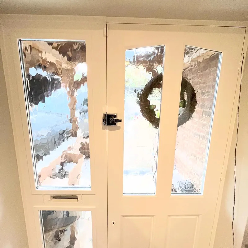 A cream-painted front door with tall textured-glass panels and a matching glazed side panel, seen from inside the hallway