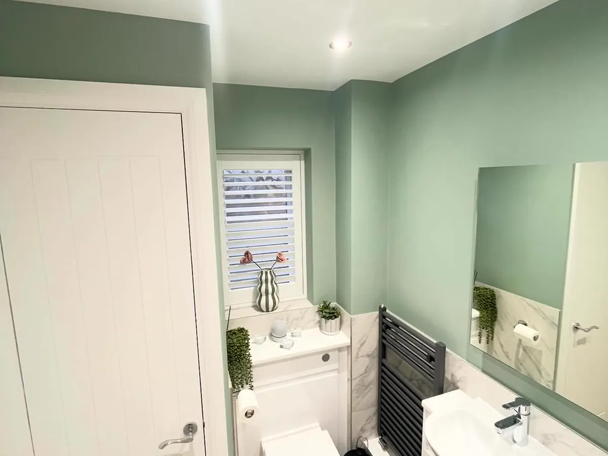 Finished bathroom decorated in sage green with a white vanity and mirror