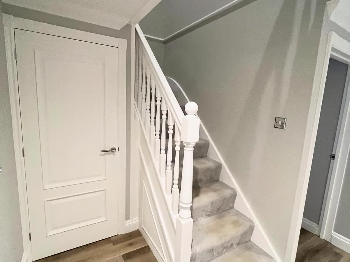 Finished staircase with a white-painted door and spindles against grey walls