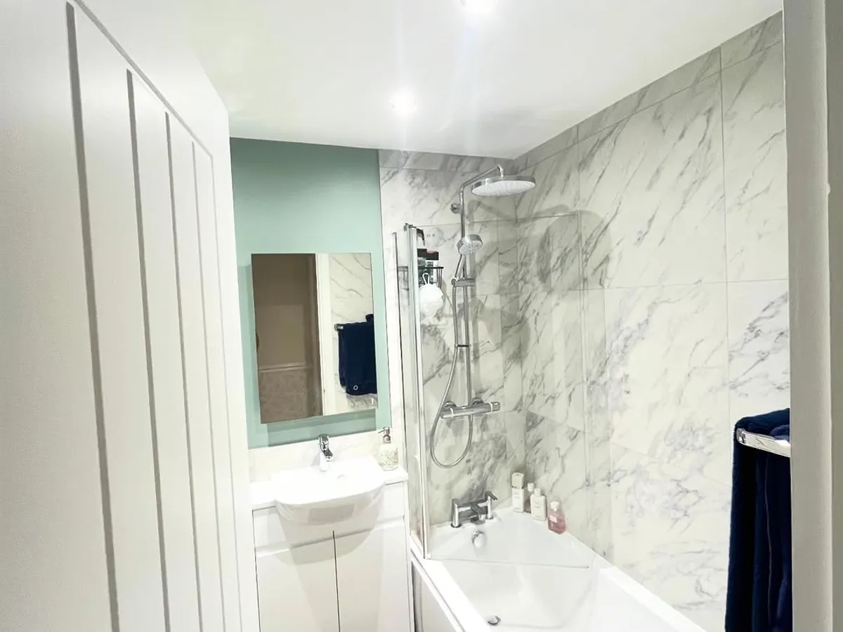 Finished bathroom with marble-effect tiling and a sage-green wall